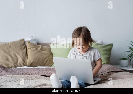 Smiling girl with down syndrome using laptop on bed at home Stock Photo