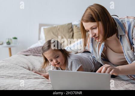Freelancer using laptop near daughter with down syndrome on bed Stock Photo