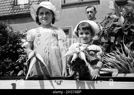 Zwei kleine Mädchen auf dem firmeneigenen Festwagen des Rettich Versands Hanacker beim Festumzug zum Rettichfest in Schifferstadt, Deutschland 1930er Jahre. Parade float of the radish dispatch company Hanacker with a staff member and two little girls at the pageant of the annual radish fair at Schifferstadt, Germany 1930s. Stock Photo