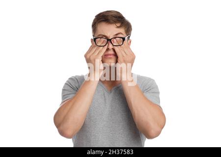 Tired young european man with eye pain, from glasses and rubs his eyes, isolated on white background Stock Photo