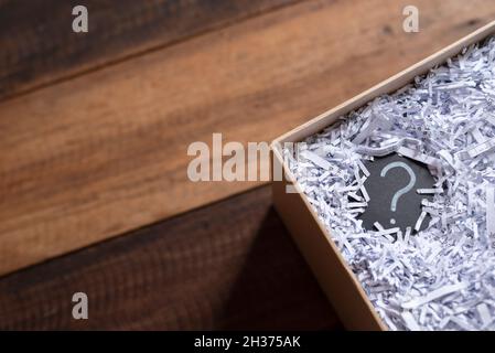 Question mark in a box with shredded paper on wooden table. Concept of suprise, delivery, shipment and questions Stock Photo