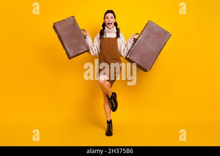 Full size photo of nice brunette optimistic curly hairdo lady hold bags wear sweater overall boots isolated on yellow background Stock Photo
