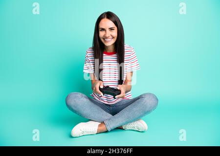 Full size photo of nice optimistic lady playstation wear t-shirt jeans sneakers isolated on teal background Stock Photo