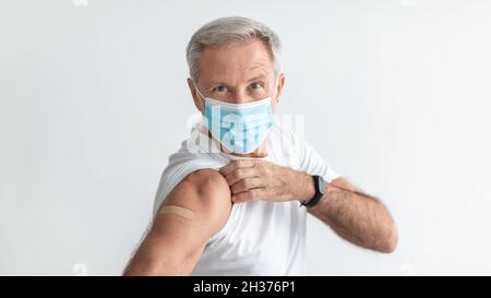 Vaccinated Senior Male Wearing Face Mask Showing Arm, Gray Background