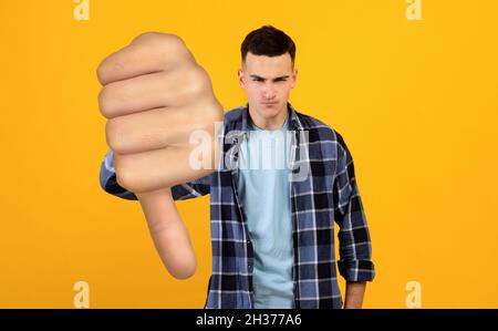 Angry young man showing thumb down on yellow Stock Photo