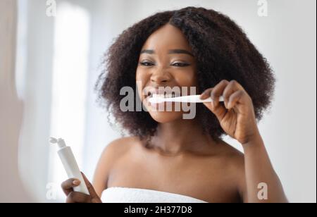 Pretty young black woman brushing teeth with toothpaste at home. Stomatology, health care concept Stock Photo