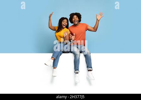 Excited black lovers sitting on horizontal white board Stock Photo