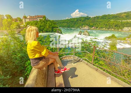 Elegant girl sitting on the panoramic view over the in the Rhine Falls in Switzerland. Swiss biggest waterfall of Europe. 490 ft wide and 75 ft high Stock Photo