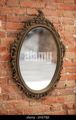 A mirror in a vintage openwork frame hangs on an old brick wall. Stock Photo