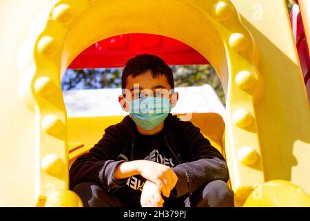 Masked boy in the park. Brunette boy in black hoodie and blue mask plays in the park. Front view. Selective focus Stock Photo