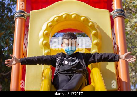 Masked boy in the park. Brunette boy in black hoodie and blue mask spread his hands to the side. Front view. selective focus Stock Photo