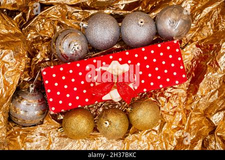 Christmas decorated gift with red and white dots on paper with red tassels and Christmas tree ball decorations isolated on a shiny orange background Stock Photo