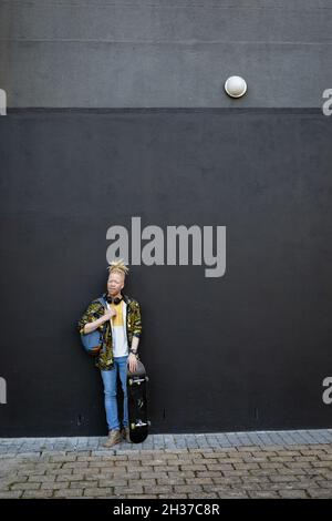 Portrait of happy albino african american man with dreadlocks holding skateboard Stock Photo