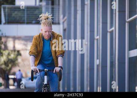 Thoughtful albino african american man with dreadlocks riding bike Stock Photo