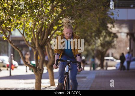 Thoughtful albino african american man with dreadlocks riding bike Stock Photo