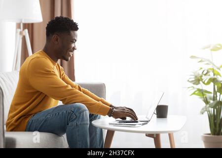 Black man freelancer sitting on couch at home, using laptop Stock Photo