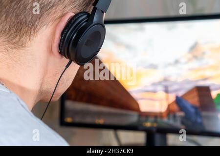 Rear view of a young man with headphones playing a video game on a computer at home Stock Photo