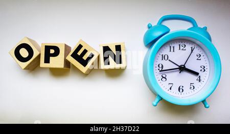 Open, text on wooden cubes, next to alarm clock on white background Stock Photo