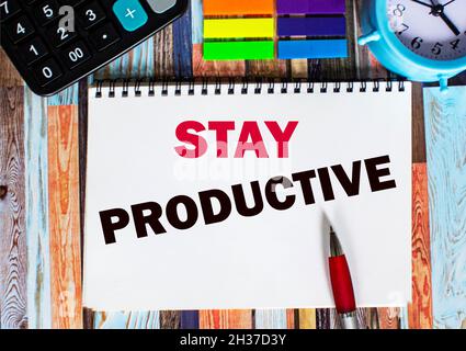 Text Stay productive written on a notepad in the office with surroundings such as a calculator, sticky notes, alarm clock and pen. Stock Photo
