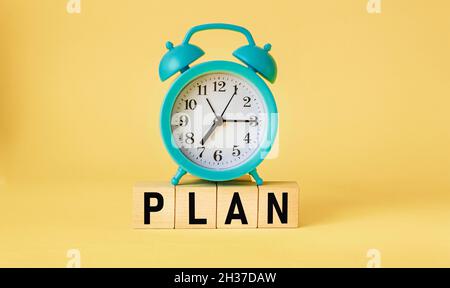 PLAN word made from building blocks isolated on yellow background with alarm clock Stock Photo