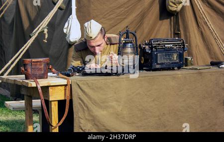 Minsk, city holiday on September 8, 2018. A male soldier sits at a table and types on a typewriter, next to war trophies. An animation of the reconstr Stock Photo