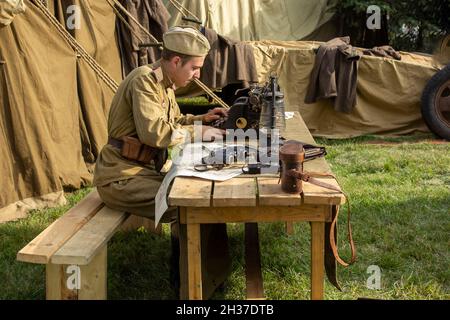 Minsk, city holiday on September 8, 2018. A male soldier sits at a table and types on a typewriter, next to war trophies. An animation of the reconstr Stock Photo