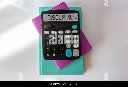 Disclaimer writing on the display of the calculator, which lies on notepads and a white background. Stock Photo