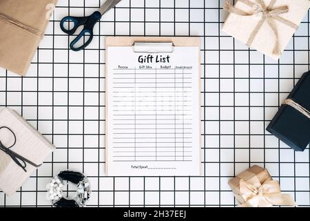 Modern flat lay with holiday gift list pintables. Keeping track gifts. Clipboard with paper gift list, wrapped boxes and wrapping tools on white Stock Photo