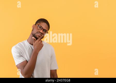 Pensive african american man looking aside at free space and touching chin, thinking about offer over yellow background Stock Photo