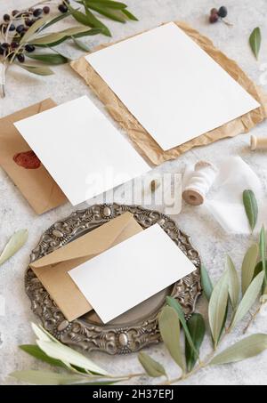 Wedding invitation cards and envelopes on a marble table decorated with olive branches close up. Elegant modern template with paper cards set. Mediter Stock Photo