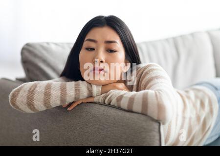 Portrait Of Lonely Upset Young Asian Female Lying On Couch At Home Stock Photo