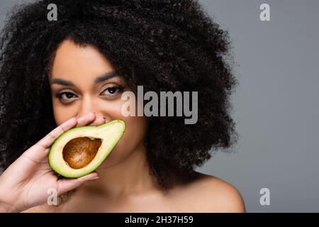 pretty african american woman holding half of fresh avocado near face isolated on grey Stock Photo