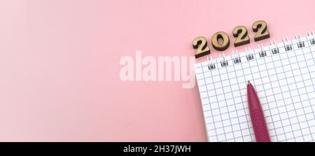 Wooden numbers 2022. Notepad on a spring. Notepad and Pen on Pink. Pink Pen. Spiral spiral checkered sheets. Stock Photo