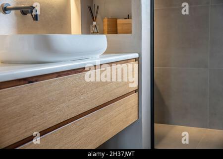 Bathroom interior modern minimal design. Round sink basin on white marble counter, black taps on grey wall, Wooden storage drawer and decoration. Stock Photo