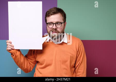 Strange man with glasses holds a letterhead, white board, ad space or notice. Colorful background. Stock Photo