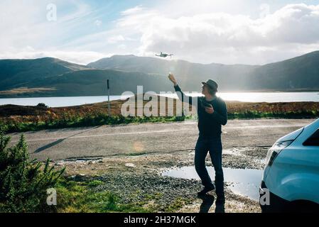 a man flying a mini mavic drone over the NC 500 route in the scottish highlands with a lake and mountains in the background Stock Photo
