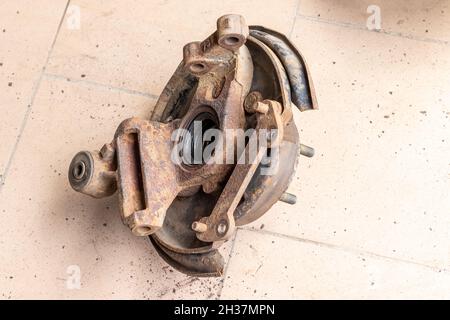 Old, used, rusty rear hub, inner part without brake disc, on the beige tiled floor of the workshop Stock Photo