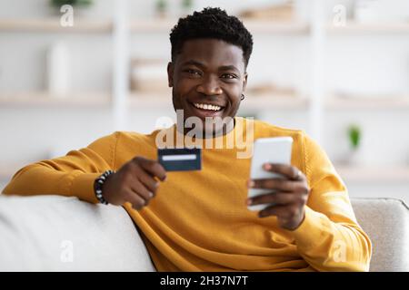 Happy young black man using cellphone and holding credit card Stock Photo