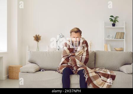 Man freezing and shivering in his cold house in winter because of broken thermostat Stock Photo
