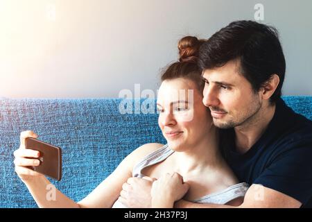 Cheerful couple with smartphone hugging and smiling. Man and woman, family of two, call friends or parents online, take selfies, watch positive videos Stock Photo
