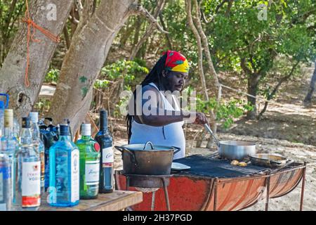 Rastafari cooking meal on barbecue at beach bar at Anse La Roche on Carriacou, island of the Grenadine Islands, Grenada in the Caribbean Sea Stock Photo