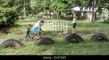 Three kids playing on old truck tires in Playa del Coco, Costa Rica. Stock Photo