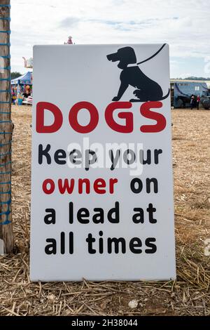 Sign reading Dogs Keep your Owner on a Lead at all times. Amusing, humorous sign at a horse event, UK Stock Photo