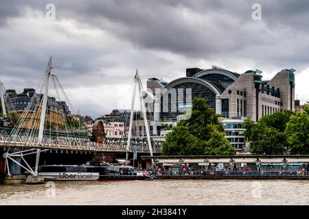 An Uber Boat Passes Under The Hungerford/Golden Jubilee Bridges With Charing Cross Station In The Backround, London, UK. Stock Photo