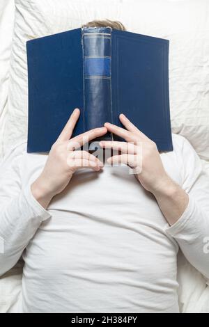 Man in pajamas fell asleep while reading with a large book on his face. Education concept. Top view. Close-up.  Stock Photo