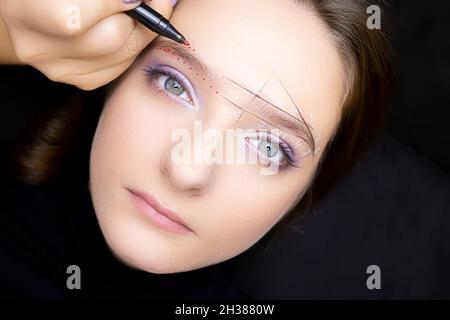 the model lies on the procedure of marking the eyebrows before correction and coloring Stock Photo