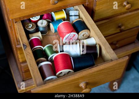 Sewing drawer with spools of thread.  Wood sewing cabinet with coloured thread. Stock Photo