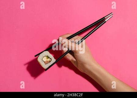 Woman holding chopsticks with tasty maki roll on color background Stock Photo