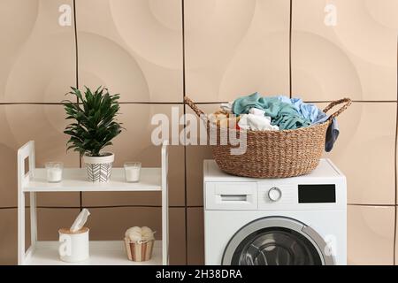 Washing machine, basket with laundry and shelving unit near beige wall Stock Photo