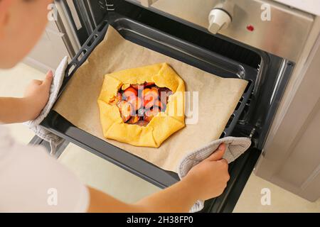 Woman putting uncooked plum galette in oven Stock Photo